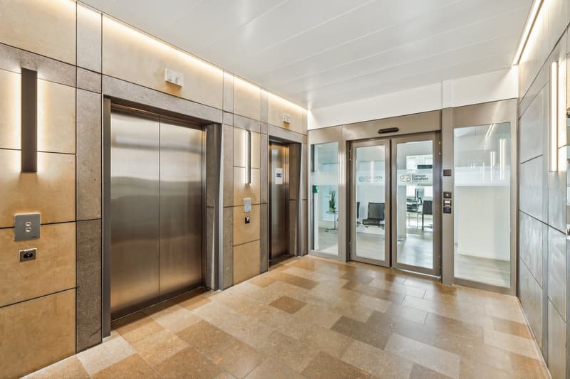 Lobby area with tiled flooring, steel elevator doors, glass doors, light fixtures, and control panels.