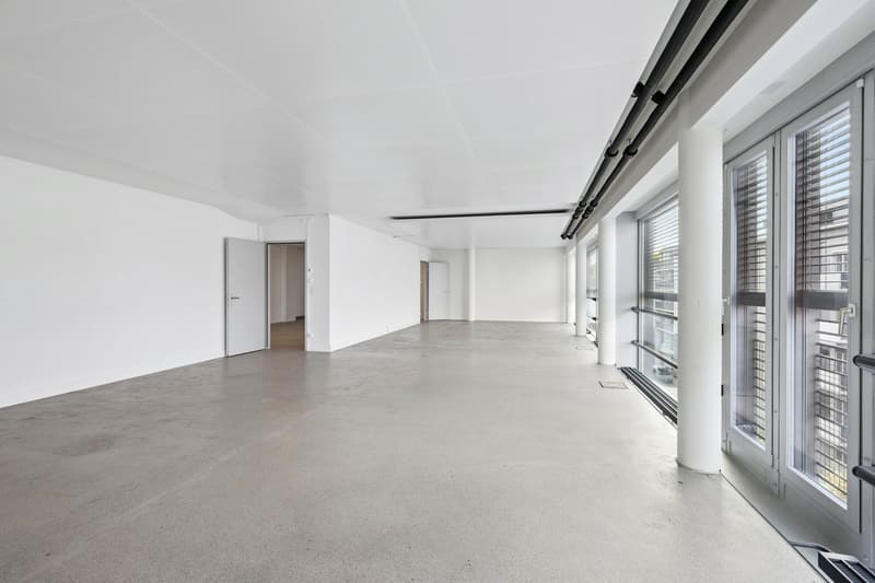 Empty room with white walls, gray floor, two doors leading to adjacent rooms, two large windows with blinds.