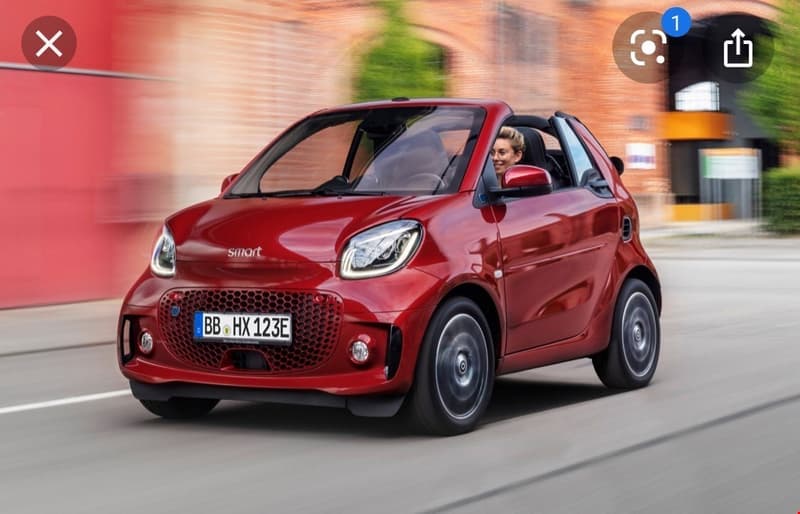 A red Smart car with license plate BB HX 123E is being driven on a road.