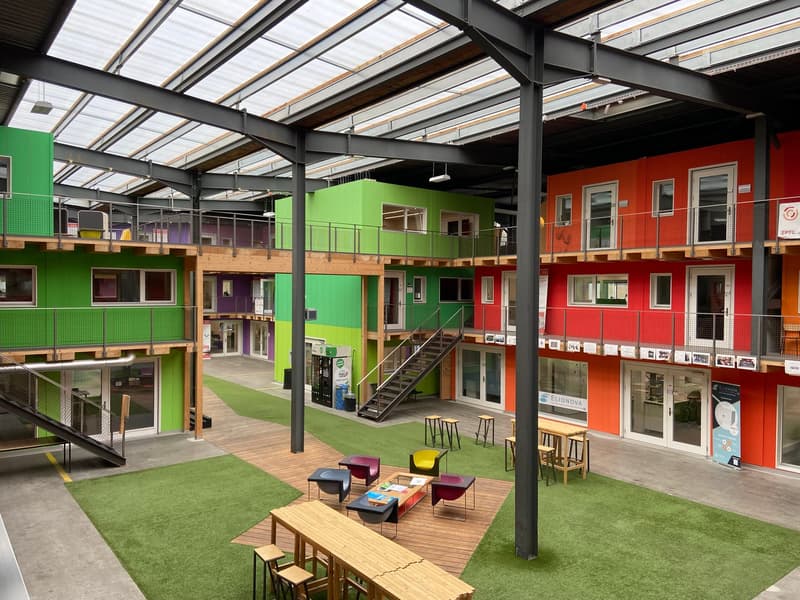 a colorfully designed office building interior with wooden stairs, artificial turf flooring, and modular building units.