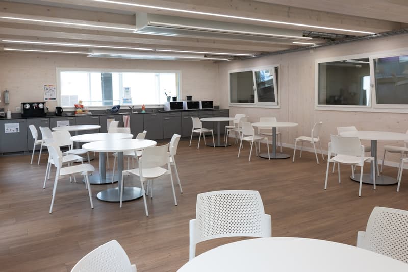 Modern kitchen with grey cabinets, white round tables, white chairs, large windows, white ceiling lights