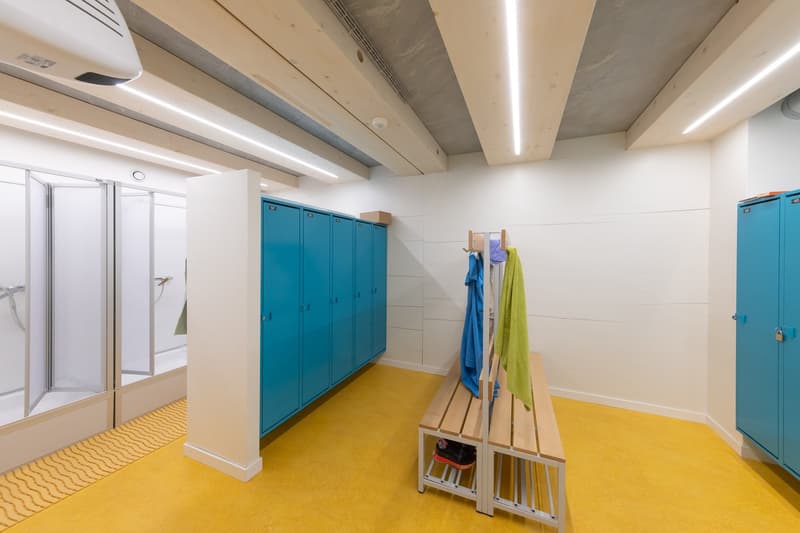Locker room with blue lockers, shower area, bench, yellow flooring, air conditioning