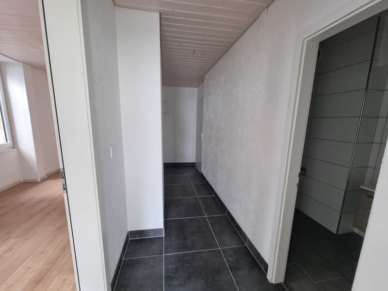Long hallway with white walls, wooden floor, black tiles, doors on both sides