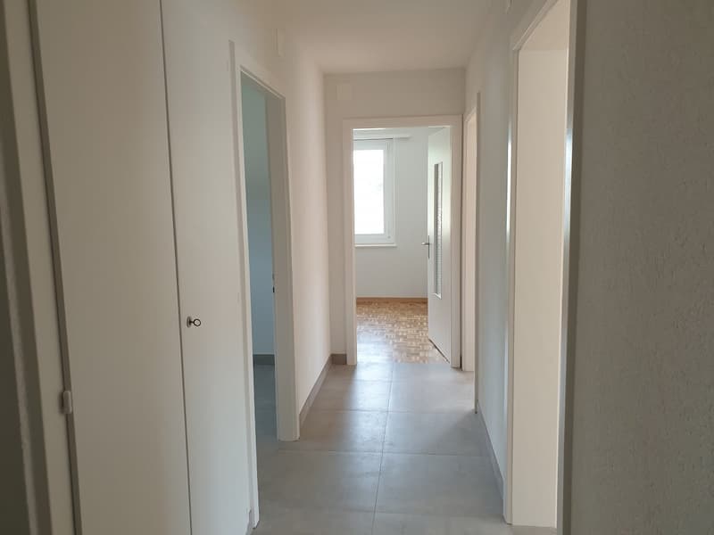 white tiled corridor, two closed doors, wooden floor visible through the second door, no furniture, empty space