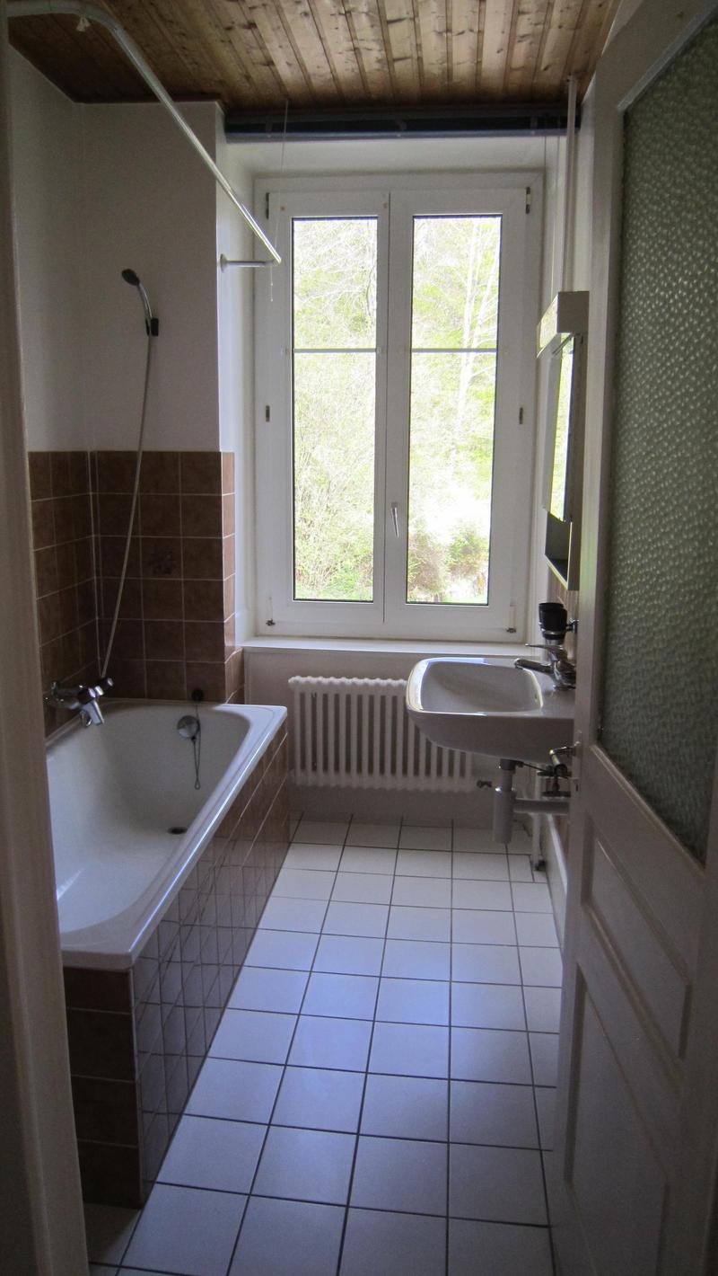 Bathroom with white tiles, bathtub, sink, mirror, and large window with view of nature
