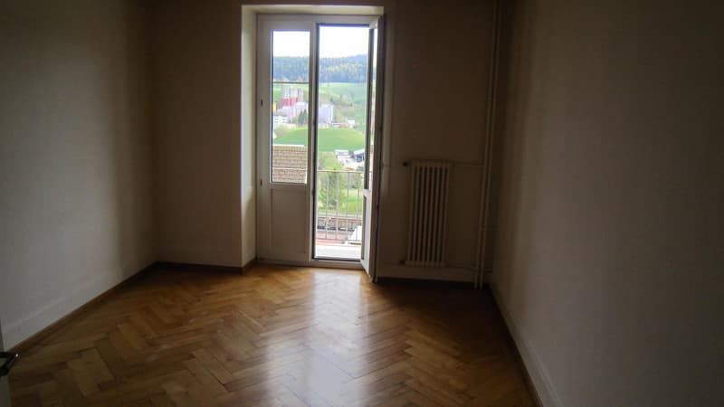 Opened door leading to balcony, wooden floor, radiator on wall, white walls