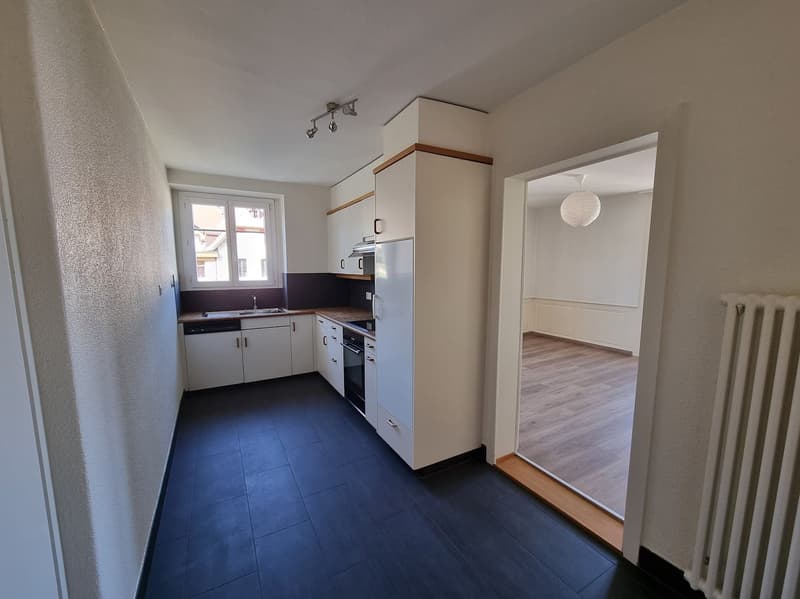 Empty kitchen with wooden floors, white cabinets, sink, dishwasher, oven, refrigerator