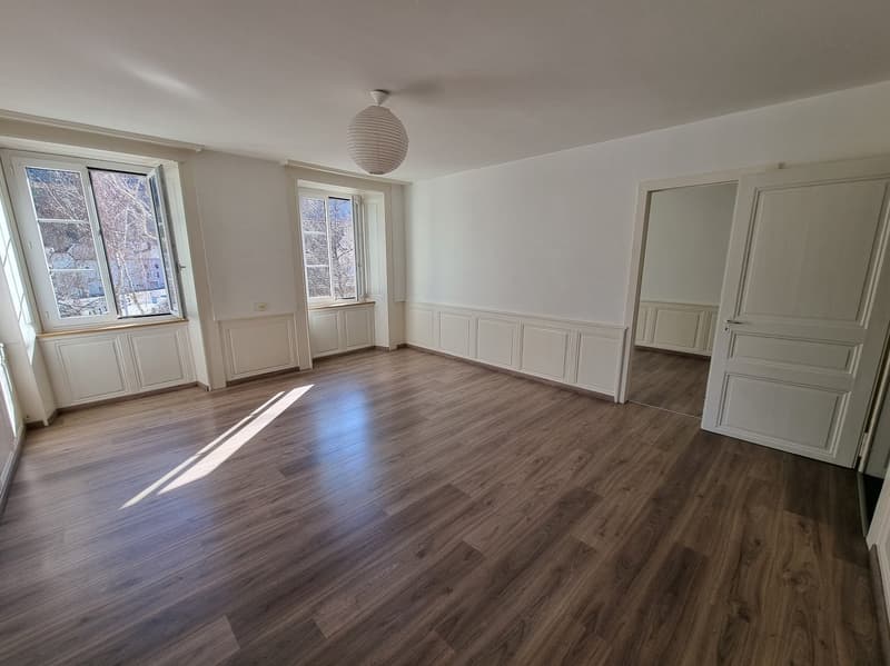 large, empty room with wooden flooring, white walls, large windows, two built-in cupboards, ceiling lamp