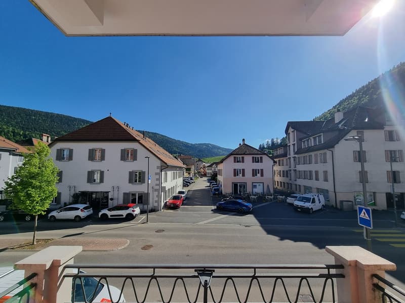Aerial view of a street with multiple buildings, cars parked, and a mountain in the background.