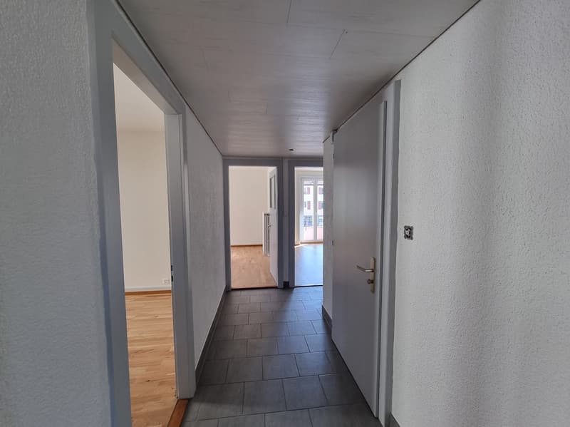 Empty hallway with tiled floor, wooden floor in some rooms, white walls, doors leading to rooms
