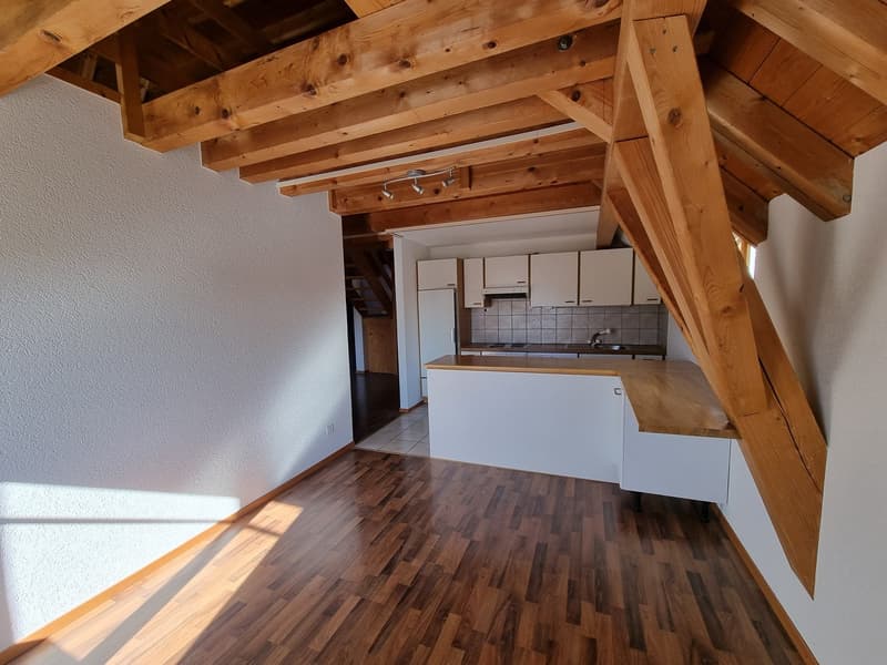 Open kitchen with wooden beams, white cabinets, wooden countertop, white walls, wooden floor
