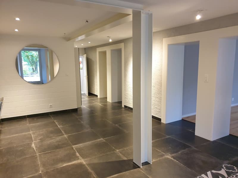 Empty room with tiled floor, white walls, round mirror, and recessed lighting