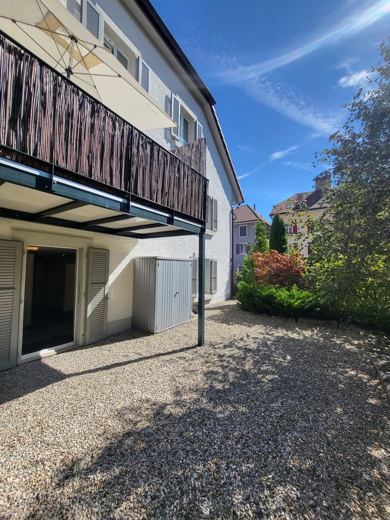 white building, balcony, gravel driveway, storage shed, trees, plants