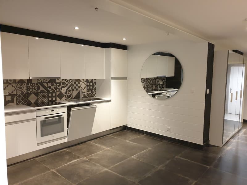 modern kitchen with white cabinets, black tiled backsplash, round mirror, dishwasher, oven, sink, tiled floor