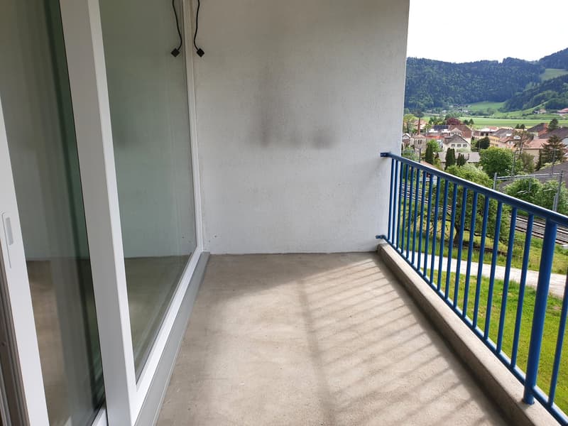 Balcony with glass door, blue railing, concrete floor, view of mountains and village