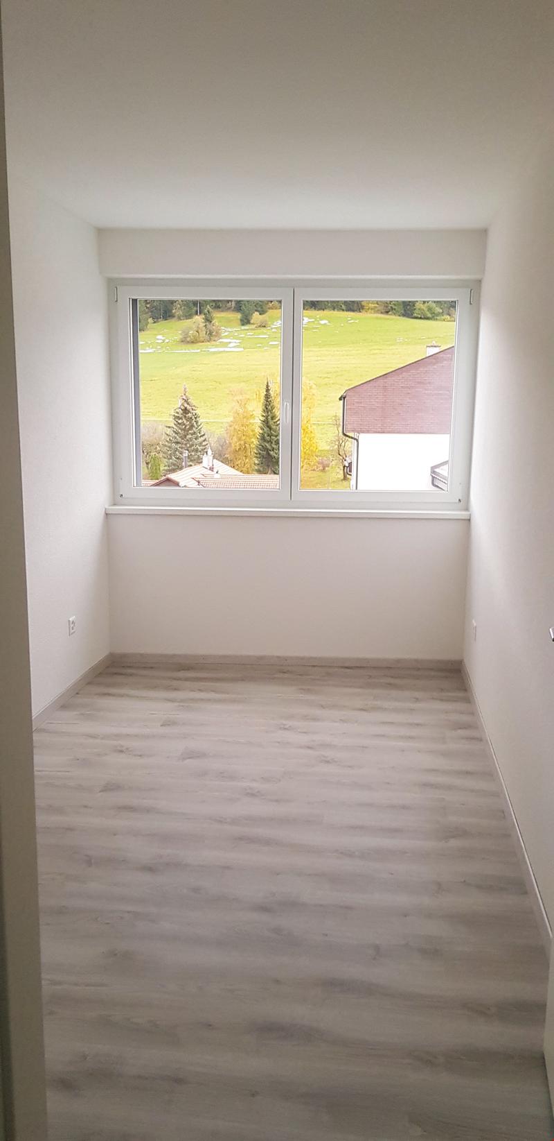 Empty room with white walls and windows, wooden floor, view of a field and houses