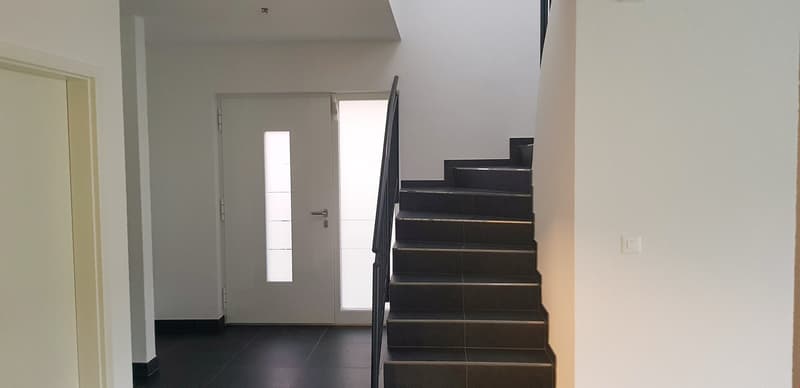 A white door with glass panels on the left, a white tiled wall, black tiled flooring, and a black staircase on the right.