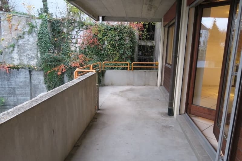 Balcony with metal railing, sliding glass door, tile flooring, open wall with plant coverage