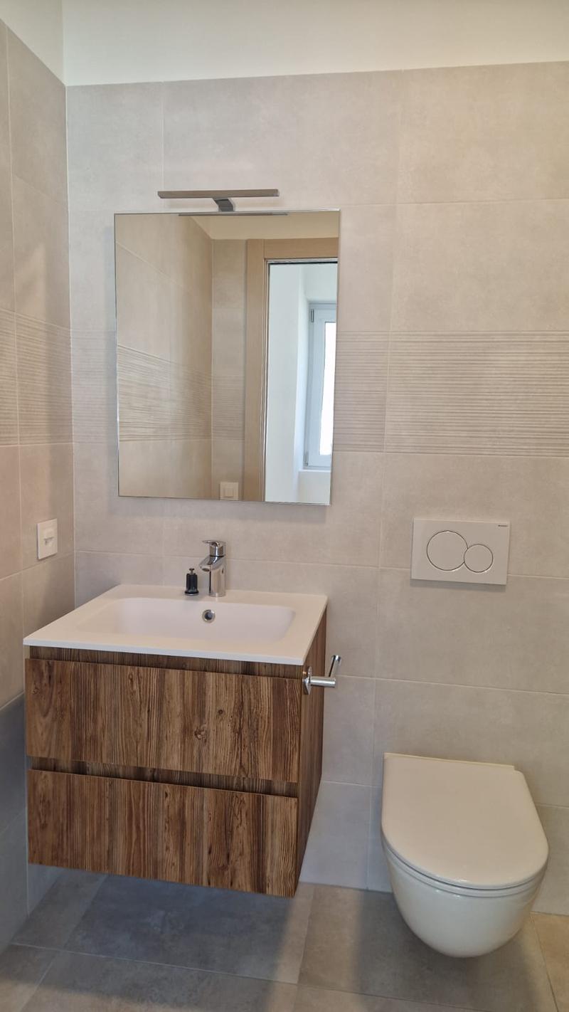 modern bathroom, tile flooring, wooden vanity, mirror, white sink, silver faucet, white toilet
