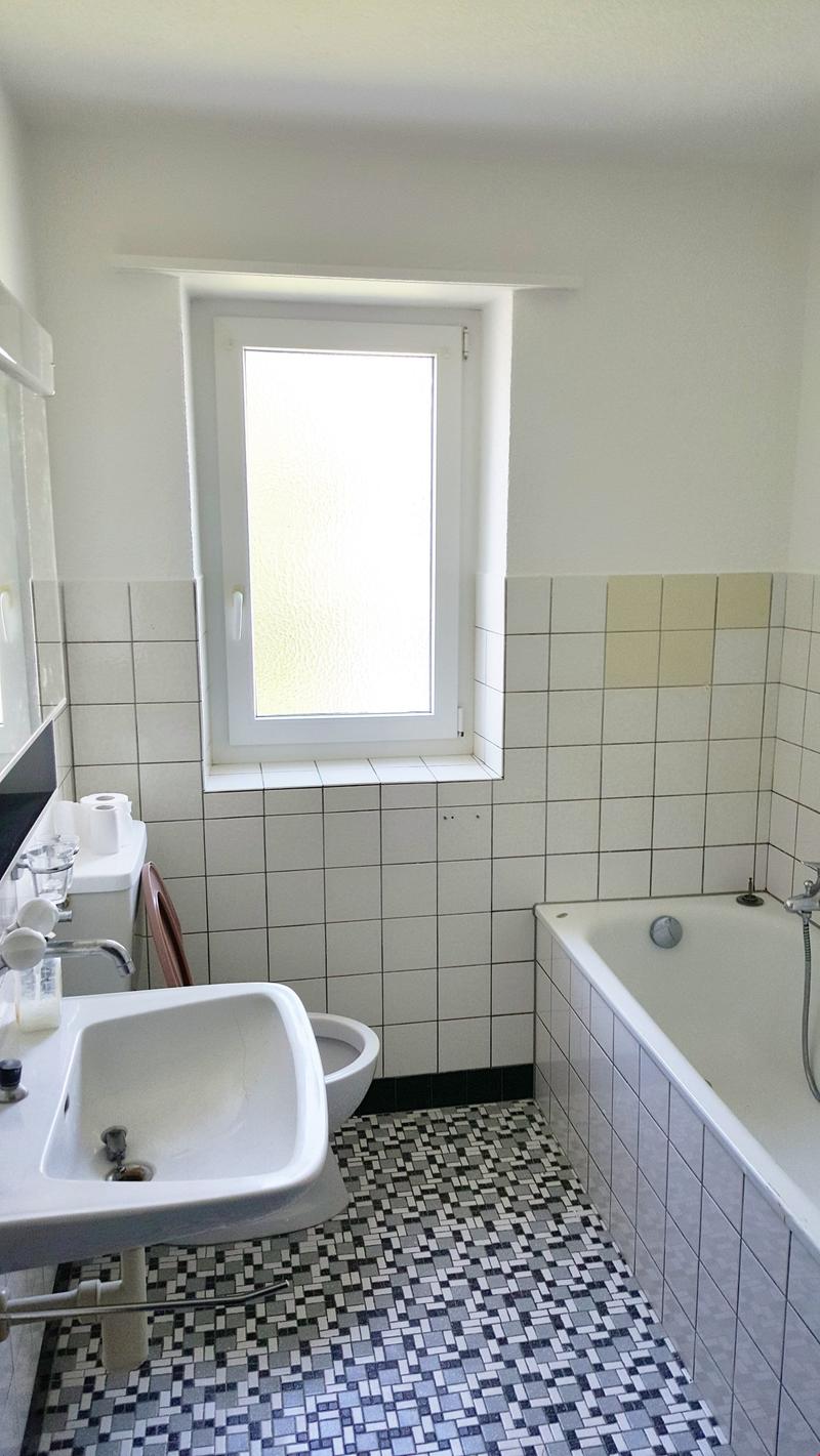 white tiled walls, white sink, white toilet, bathtub with shower, window