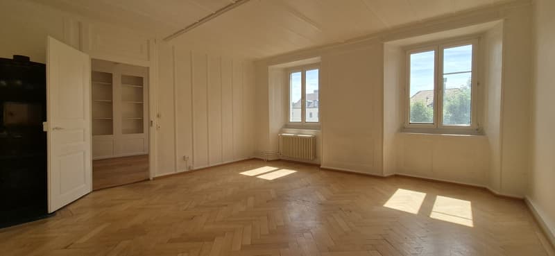 empty room, wooden floor, white walls, two windows, radiator, open door
