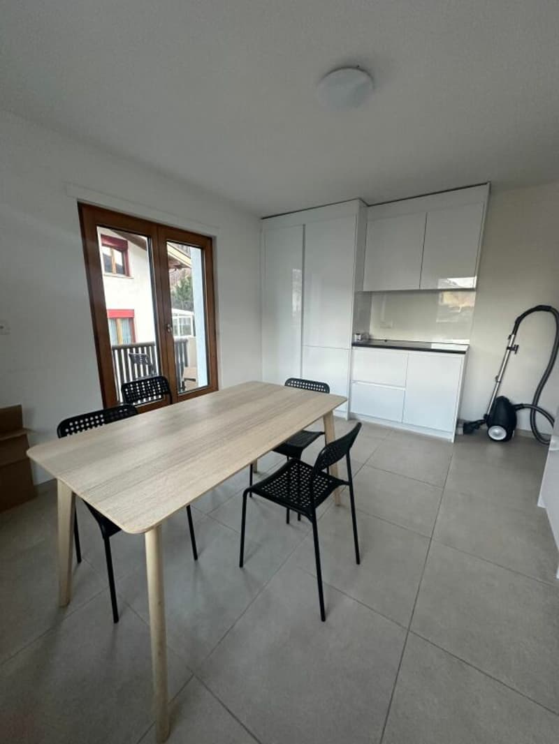 Dining area with a wooden table and black chairs, white cabinets, and a glass door leading to a balcony.