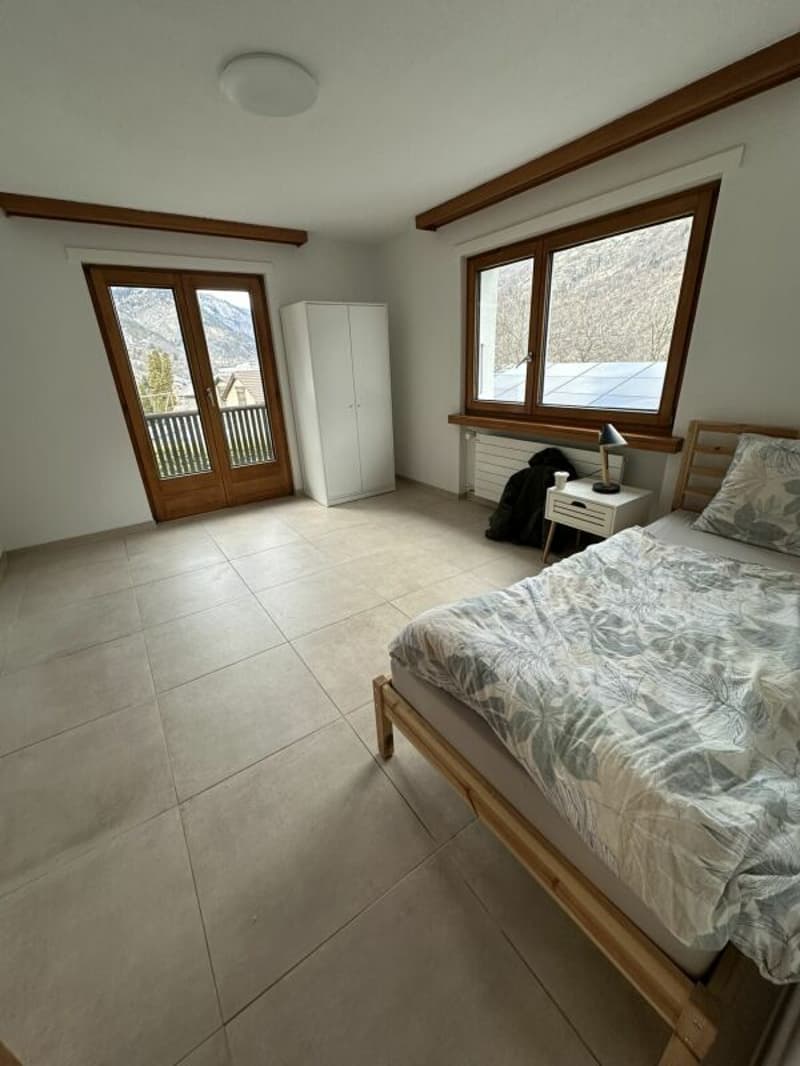 bedroom with wooden bed, white wardrobe, tiled floor, large windows, balcony, mountain view
