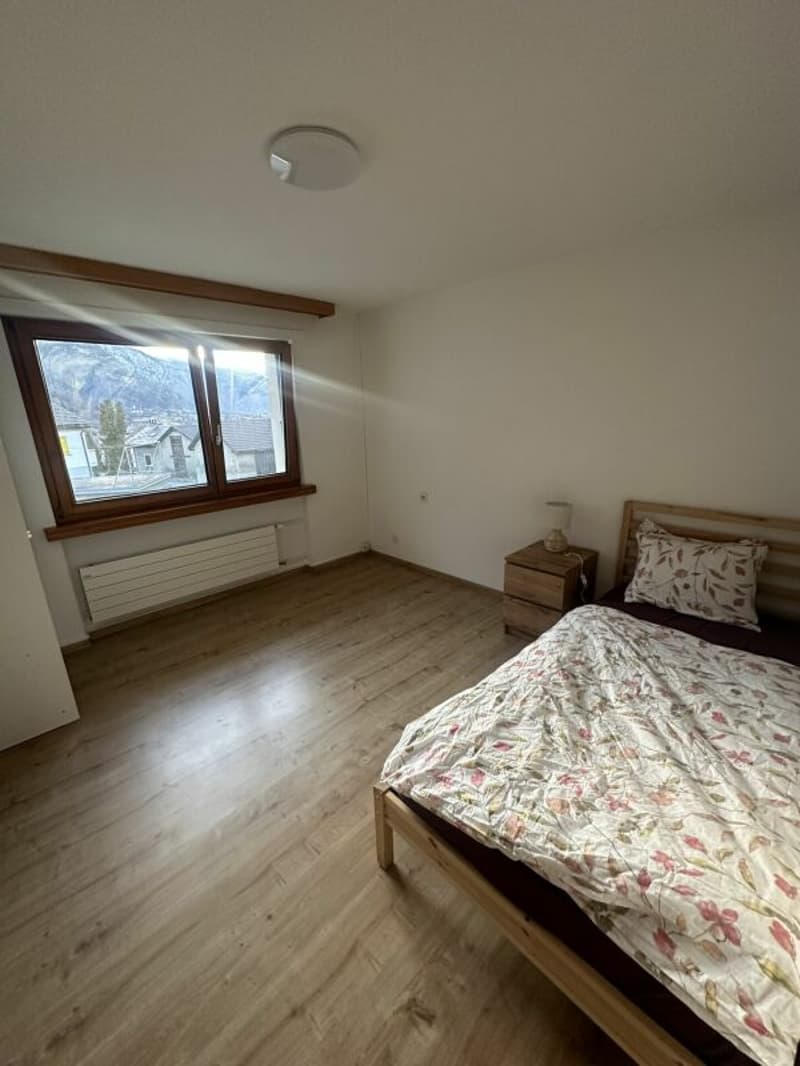 bedroom with wooden floor, bed, nightstand, lamp, window, radiator, mountain view