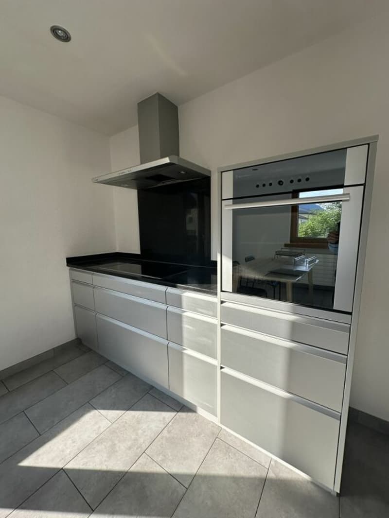 modern kitchen with stainless steel cabinets, black countertops, integrated oven and stove, extractor hood, tiled floor