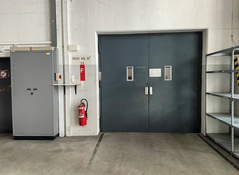 empty garage room, large gray door, fire extinguisher, metal shelves, white wall