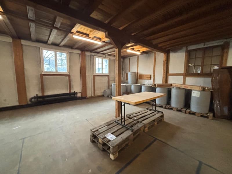 large room, wooden beams, cement floor, folding table on a pallet, storage barrels, windows