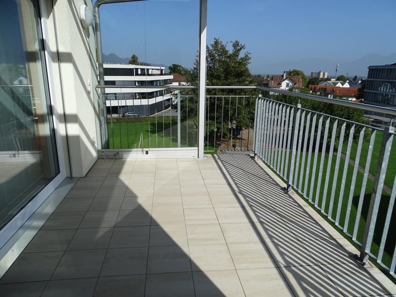 Glass doors, metal railings, tiled floor, and a view of a green lawn with trees and buildings