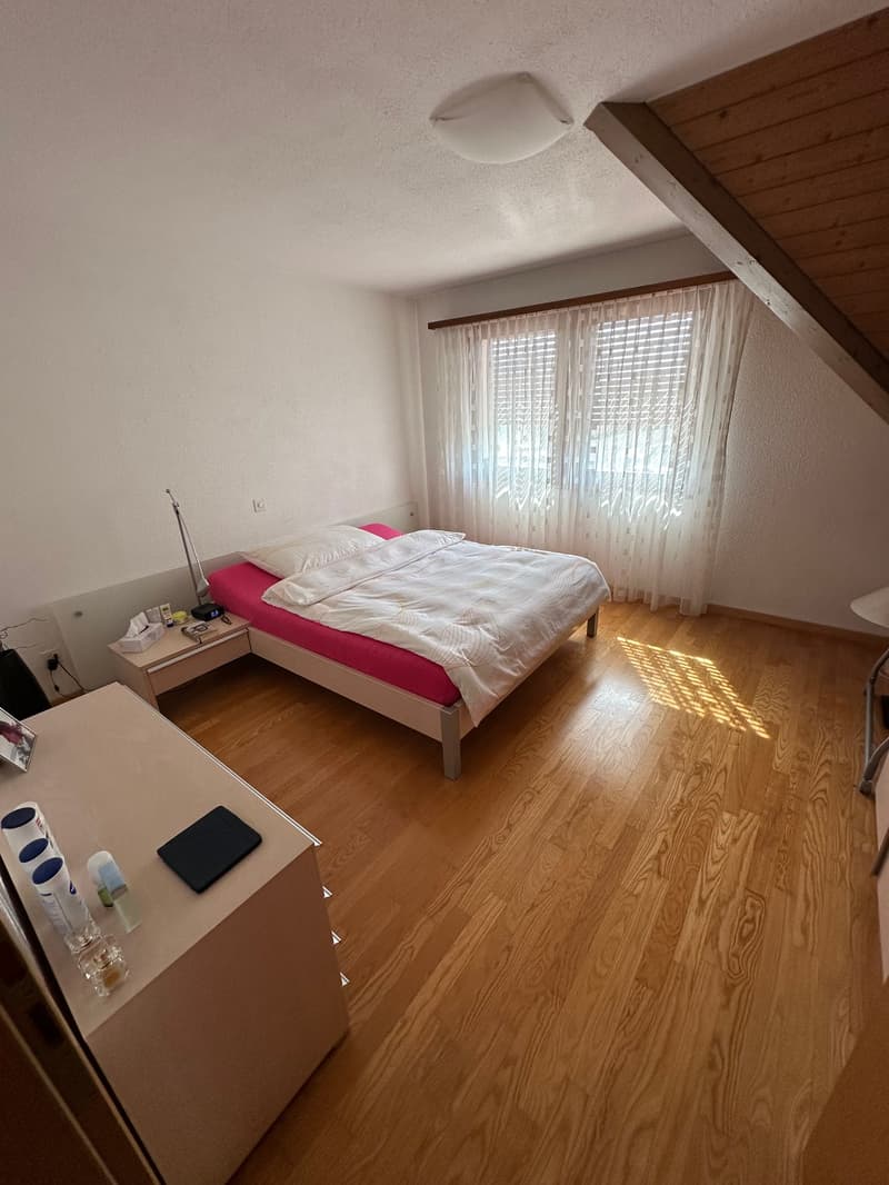 Spacious bedroom with hardwood flooring, large windows, and a pink bed frame. There appears to be a dresser or nightstand next to the bed.