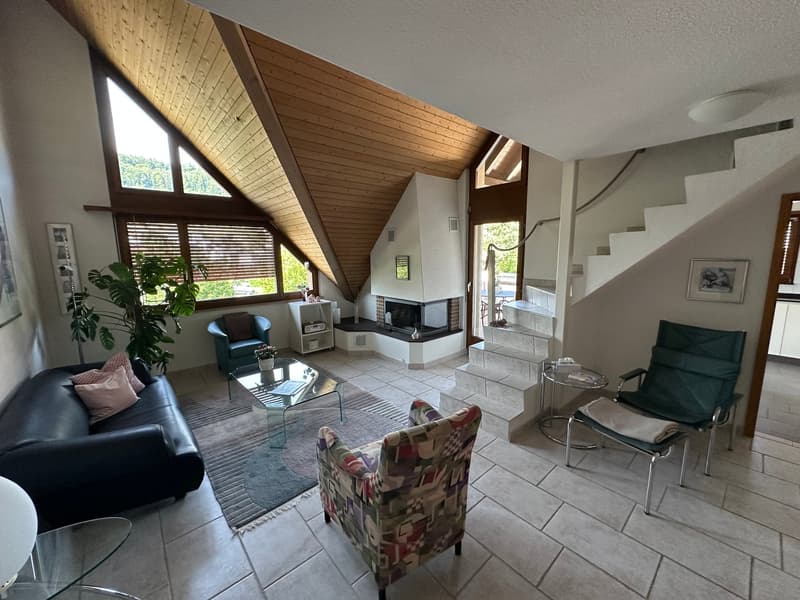 Open-concept living room with vaulted wood-paneled ceiling, large windows, tile flooring, leather sofa, armchair, coffee table, and a fireplace