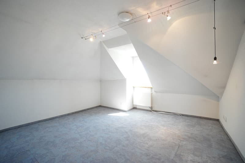 empty attic room, white walls, gray floor, angled ceiling, ceiling lighting, small window