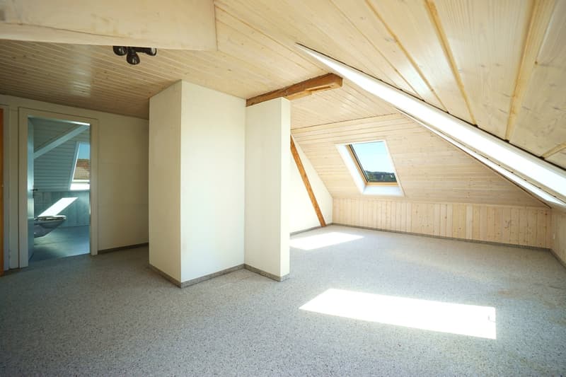 Empty attic room with white walls, wooden ceiling, exposed beams, and skylight