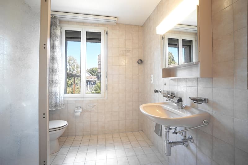 Bathroom with a toilet, sink with a mirror, and a window with a curtain.