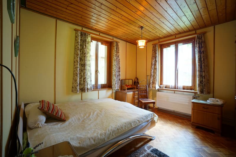 wooden ceiling, hardwood floor, a double bed with two pillows, a chair, desk, cabinet, windows with curtains, radiator