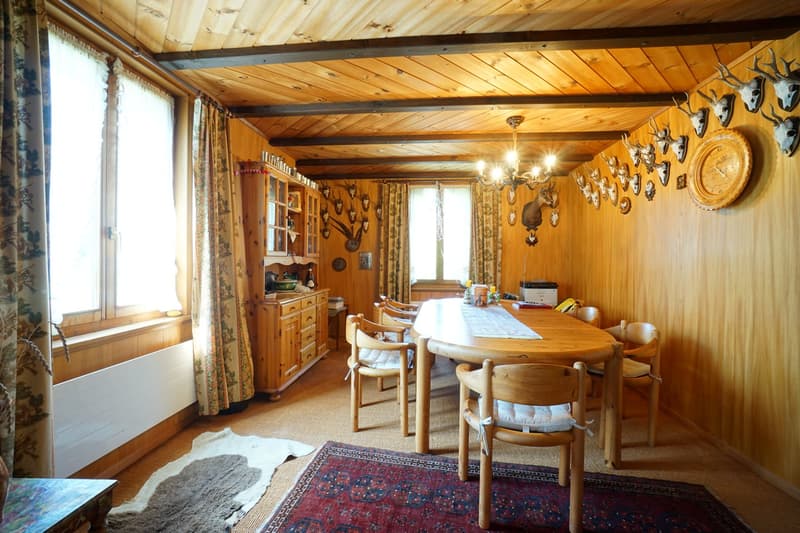 Dining room with wooden furniture, wooden beams, chandelier, wall with animal heads, large windows with curtains