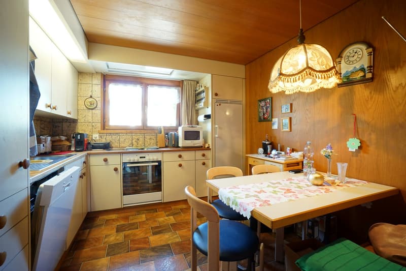 Wooden floor, white cabinets, silver and white appliances, dining table and chairs, light fixture, small window, artwork