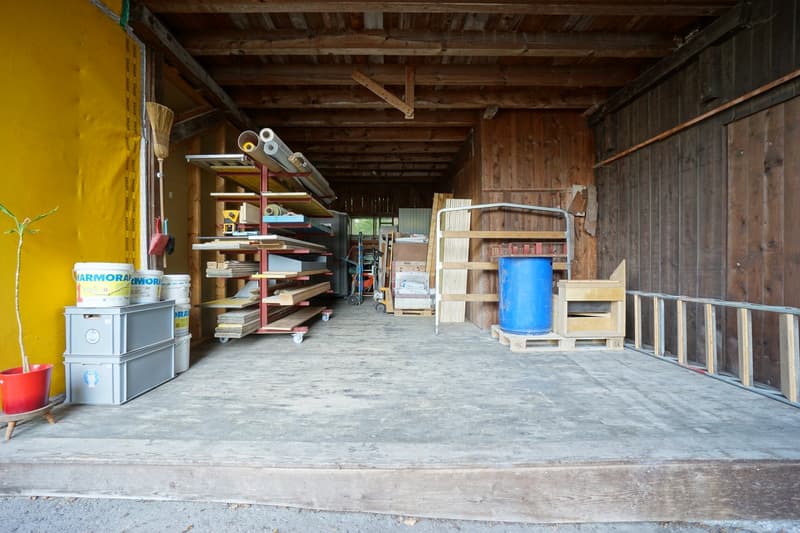 Wooden beams, large open space, shelves with building materials, barrels, trolley, plants