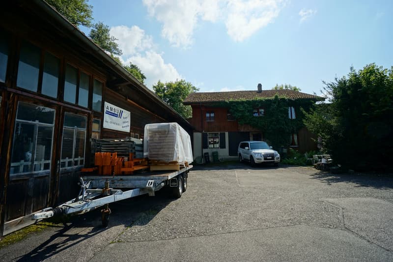 trailer loaded with materials, white SUV parked in front of house, wooden building with large windows, sign for AMSU Baugenossenschaft