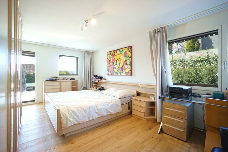 Bedroom with wooden floor, bed, desk, printer, windows, curtains, wooden cabinets, painting, lamps