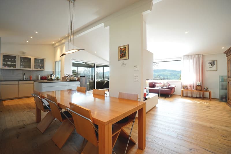 Dining area with wooden table and chairs, modern kitchen, living area with couch and window