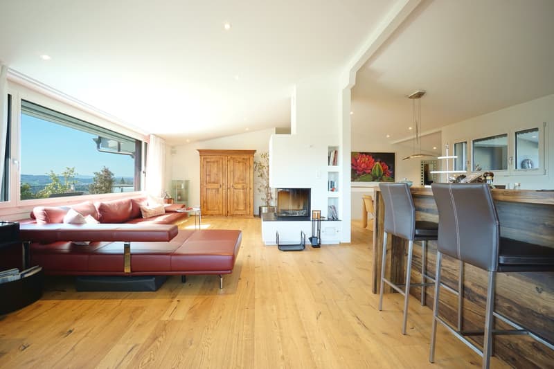 modern living room with hardwood floor, fireplace, large windows, red couch, coffee table, wooden cabinet, bar stools