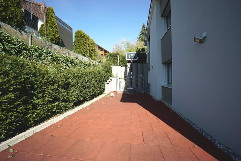 Red brick paved walkway, hedges, basketball hoop, soccer goal, building wall