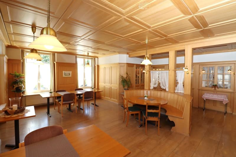 Spacious dining room with wooden paneled ceiling, large windows, wooden furniture including tables and chairs, built-in cabinets, and a fireplace