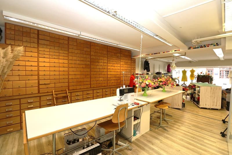 Large room with wooden storage cabinets covering one wall, a sewing machine and work table in the center, and various craft supplies and decor items throughout the space.