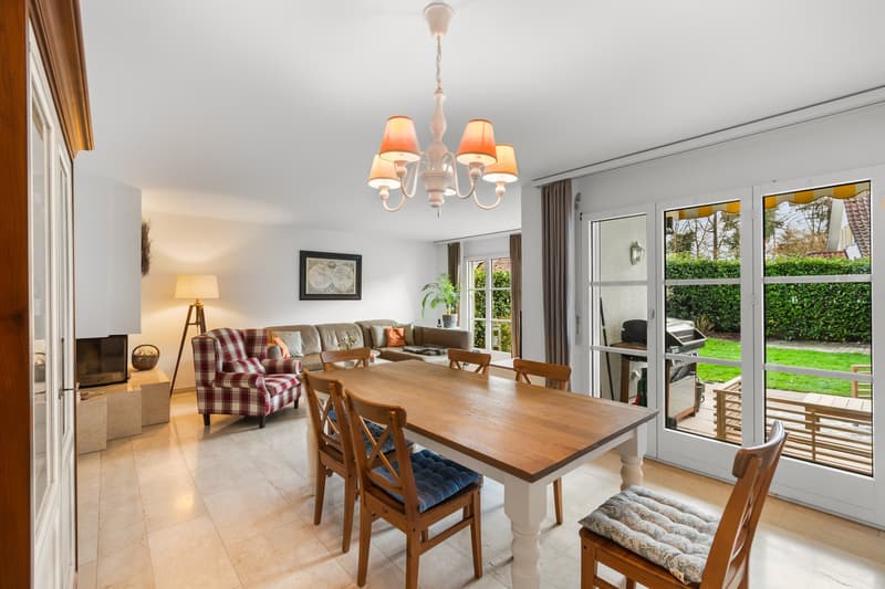 dining table with 6 chairs, living room in background, fireplace visible, large windows with terrace access, chandelier