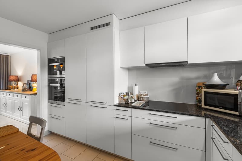 modern kitchen with white cabinets, granite countertop, built-in oven, microwave, island, and a dining table